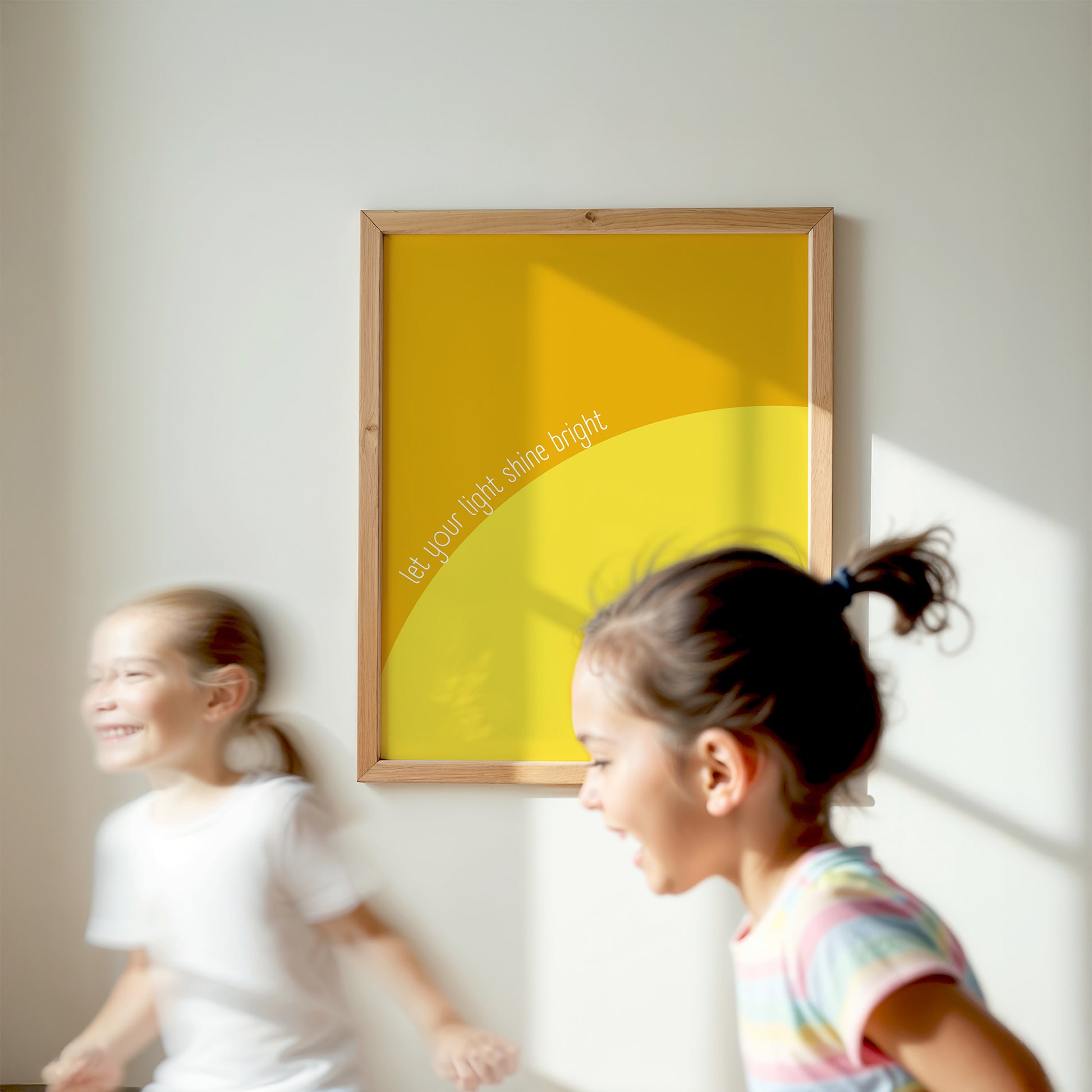 Framed LET YOUR LiGHT SHiNE BRiGHT yellow abstract poster on wall with children playing nearby in bright room.