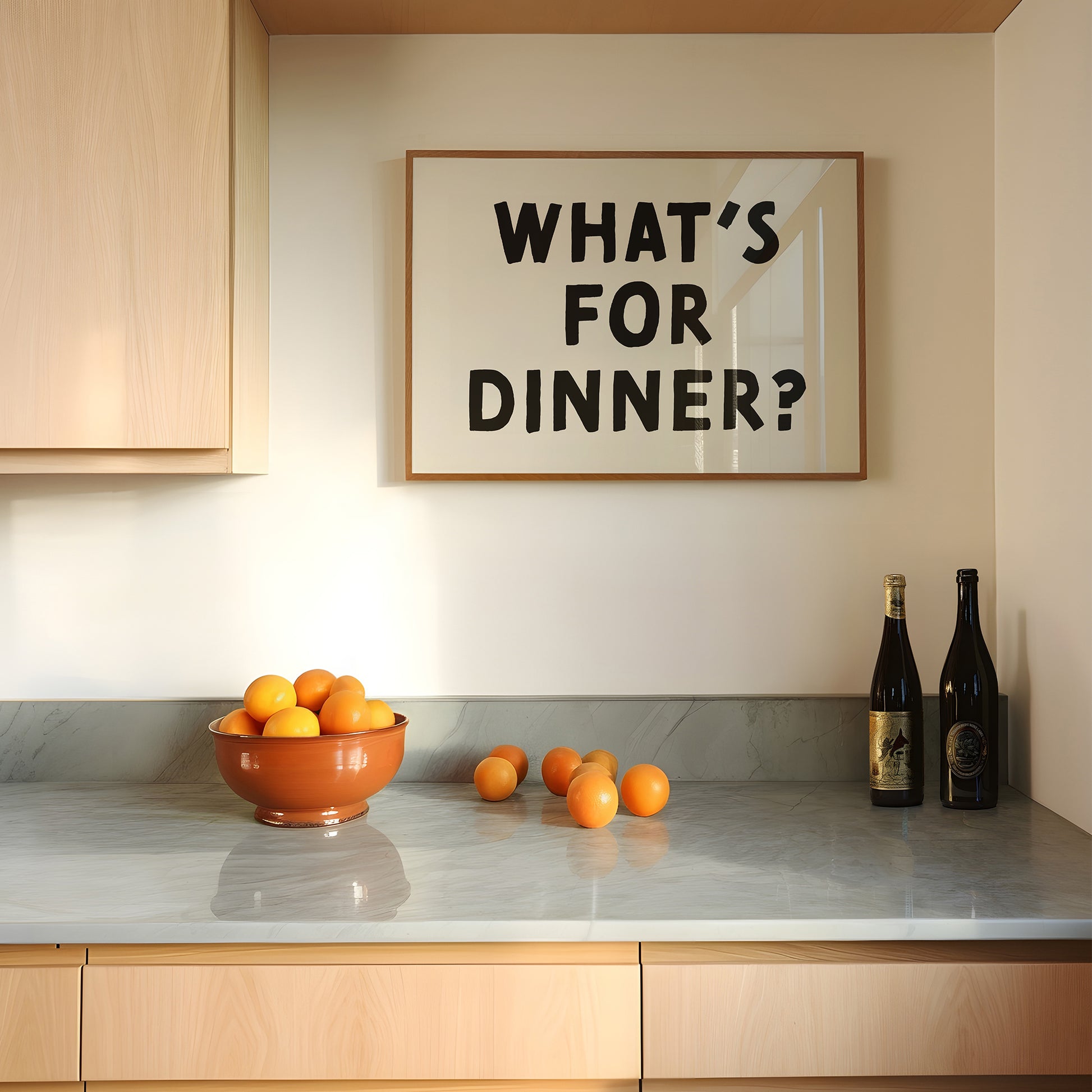 Minimalist kitchen wall art poster titled WHAT'S FOR DiNNER? in black and white displayed above a countertop with oranges.