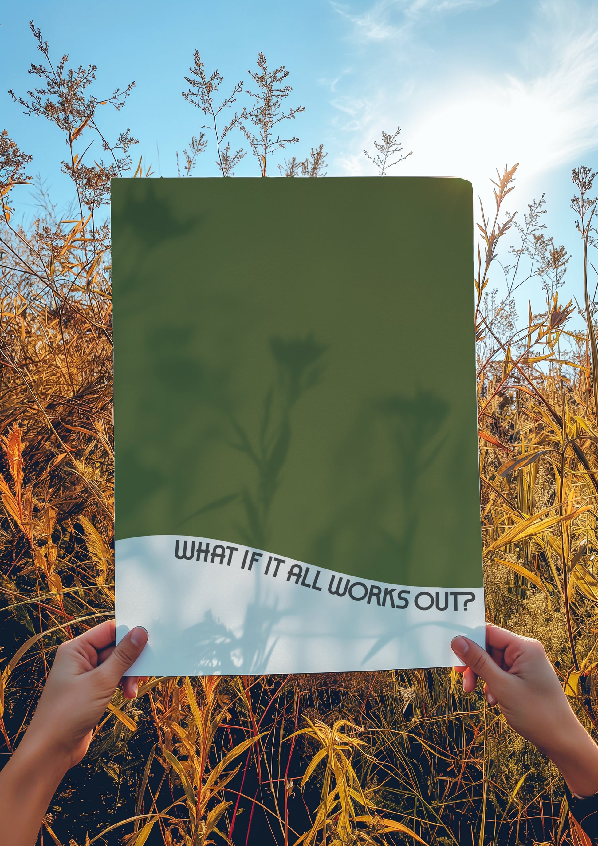 Hands holding "WHAT iF iT ALL WORKS OUT" poster with olive green and wavy text against a natural outdoor background.
