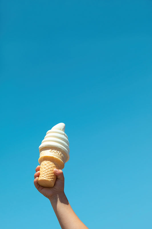 Child's hand holding soft-serve cone against clear blue sky in the product "IN FROSTiES WE TRUST" print.