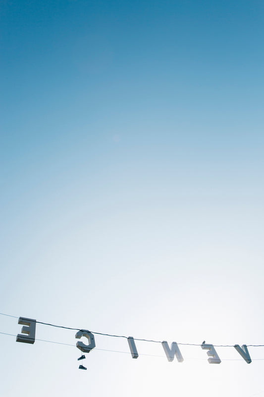 BACKWARDS features the iconic Venice sign reversed against a clear blue sky in a light-filled coastal California scene.