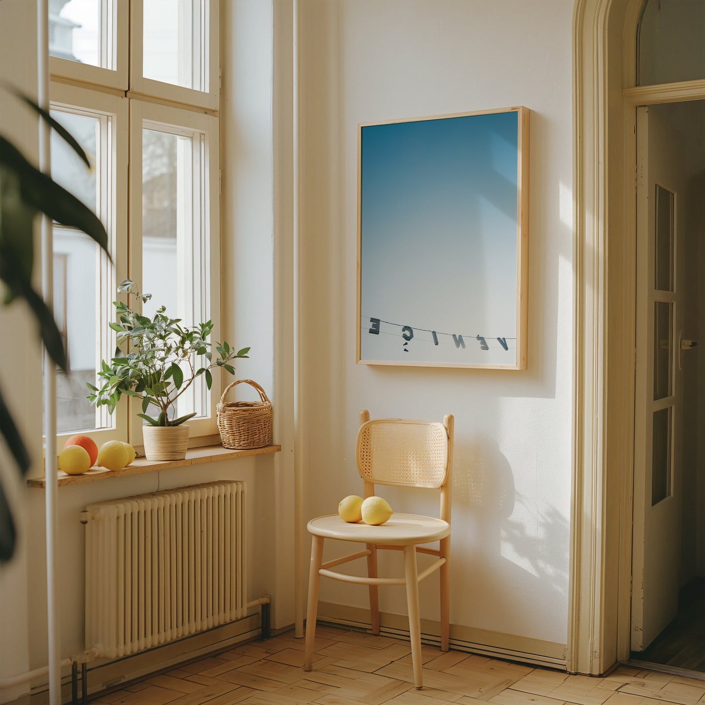 Framed "BACKWARDS" photo of reversed Venice sign against blue sky, displayed in sunlit modern interior with chair and plants.