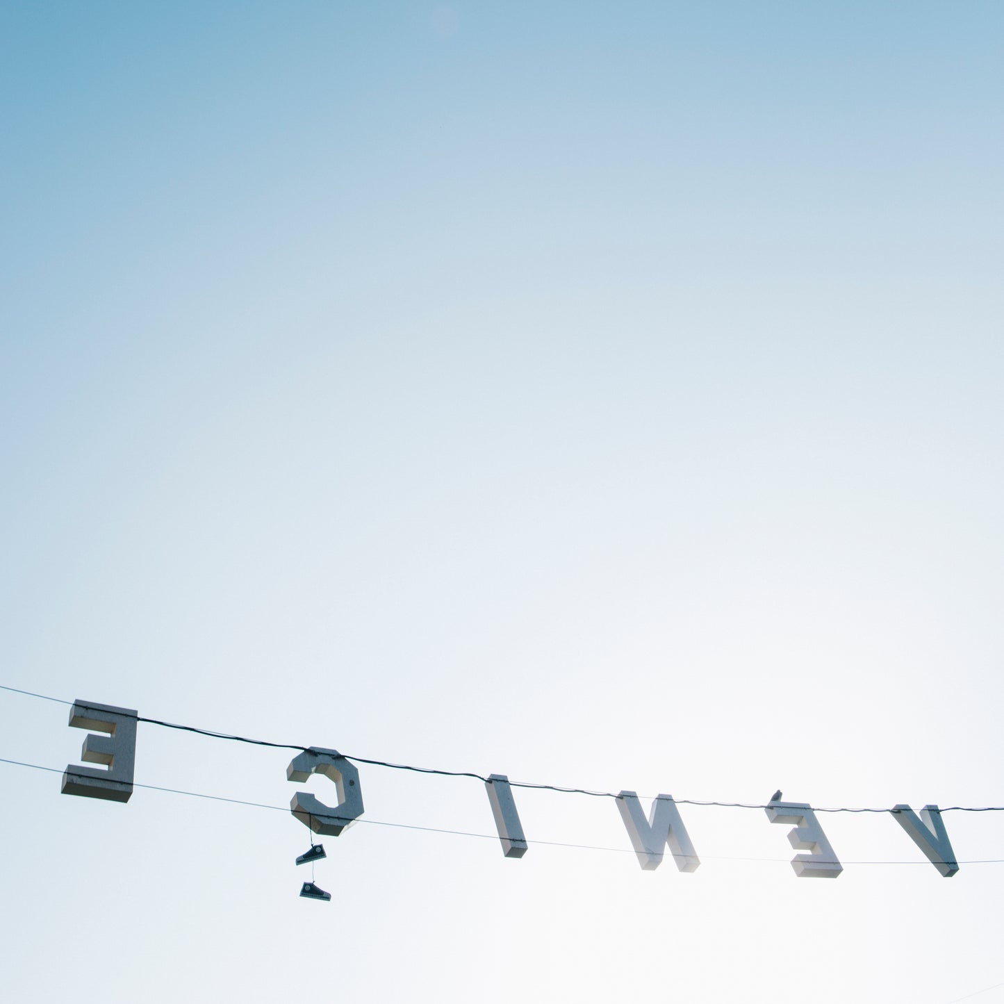 BACKWARDS featuring the Venice sign reversed against a soft blue sky, capturing a light, airy California coastal vibe.