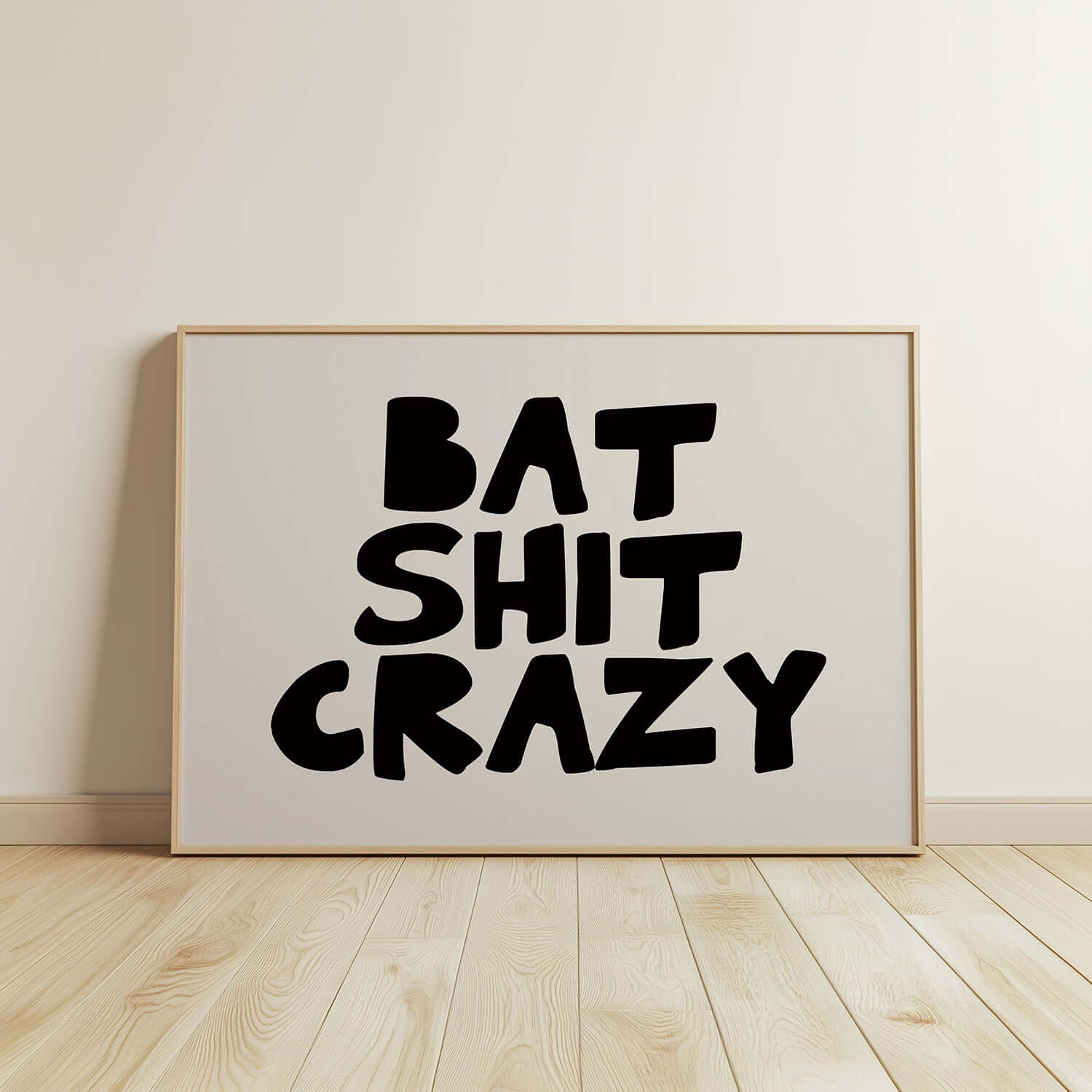Framed black and white poster with chunky hand-lettered typography reading BAT SHiT CRAZY displayed on wooden floor.