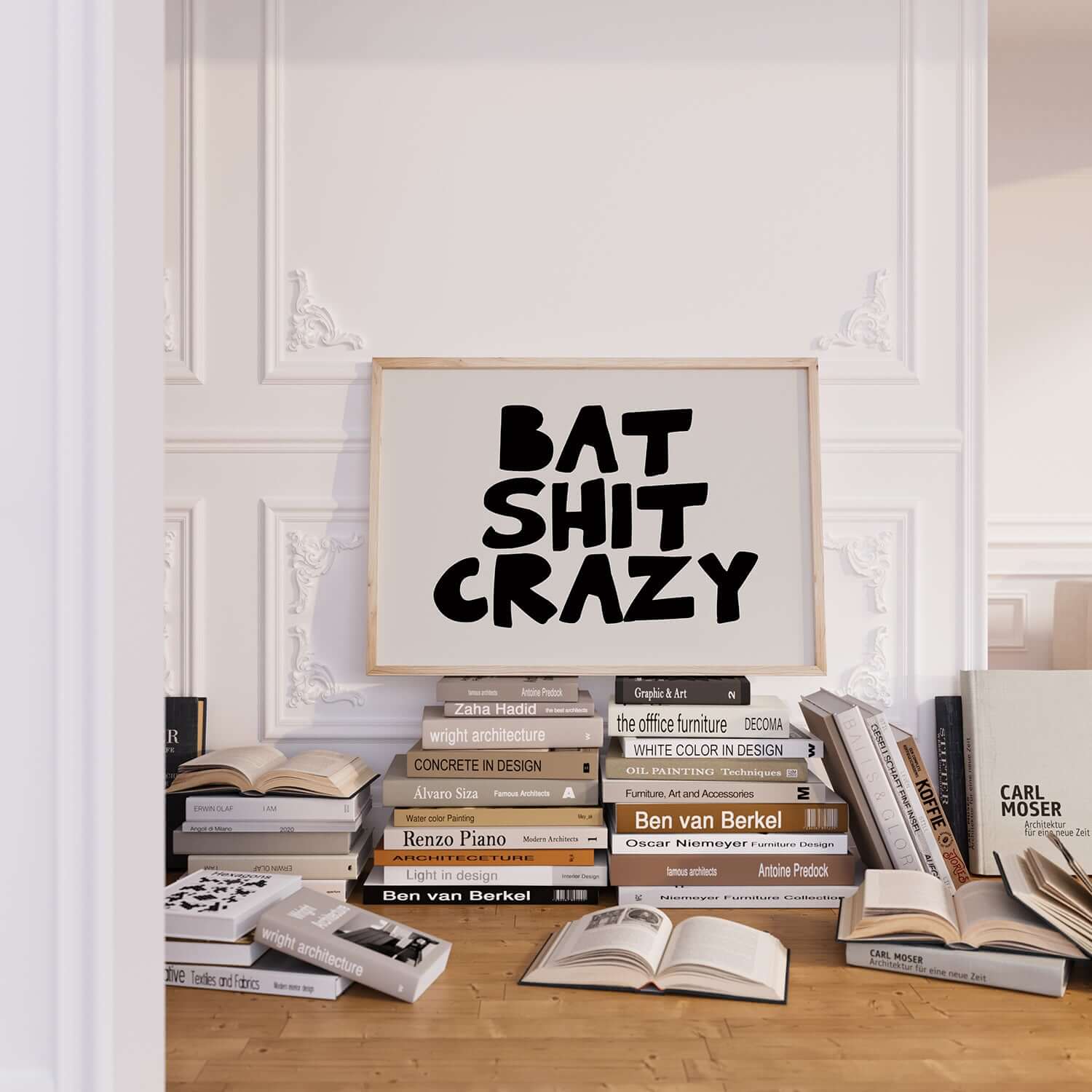 BAT SHiT CRAZY poster with bold black hand-lettered text on white, displayed above books in a stylish room.