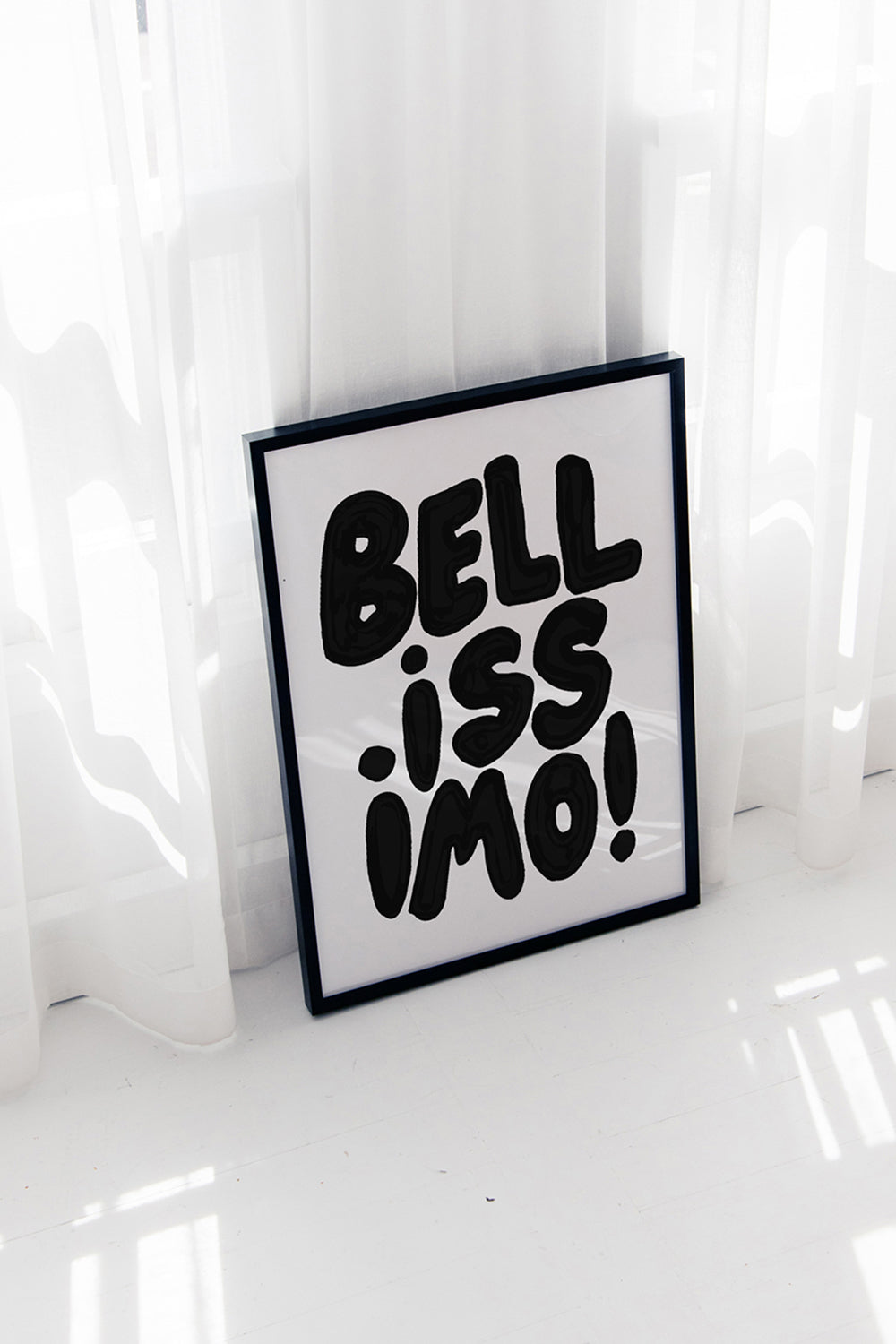 BELLiSSiMO! black & white poster with bold hand-lettered typography in black frame leaning against white curtains.
