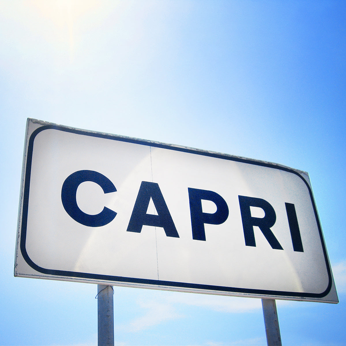 CAPRi product showing a minimalist white sign with bold black letters under a bright blue Mediterranean sky.