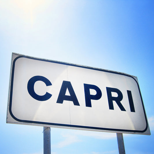 CAPRi product showing a minimalist white sign with bold black letters under a bright blue Mediterranean sky.