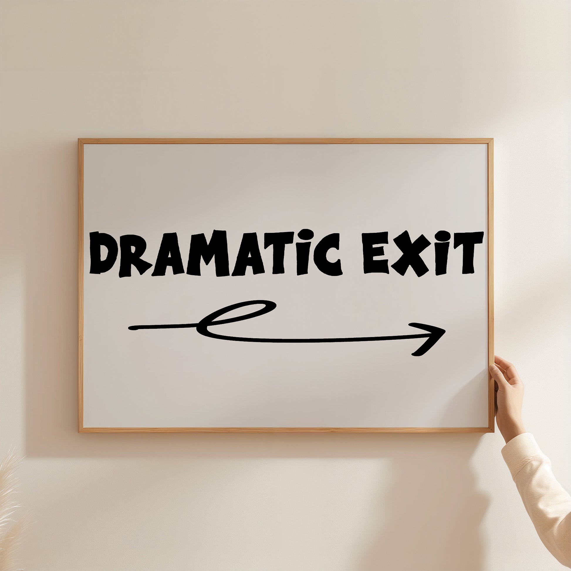 Hand holding framed poster with bold text "DRAMATiC EXiT RiGHT" and arrow pointing right on white background.