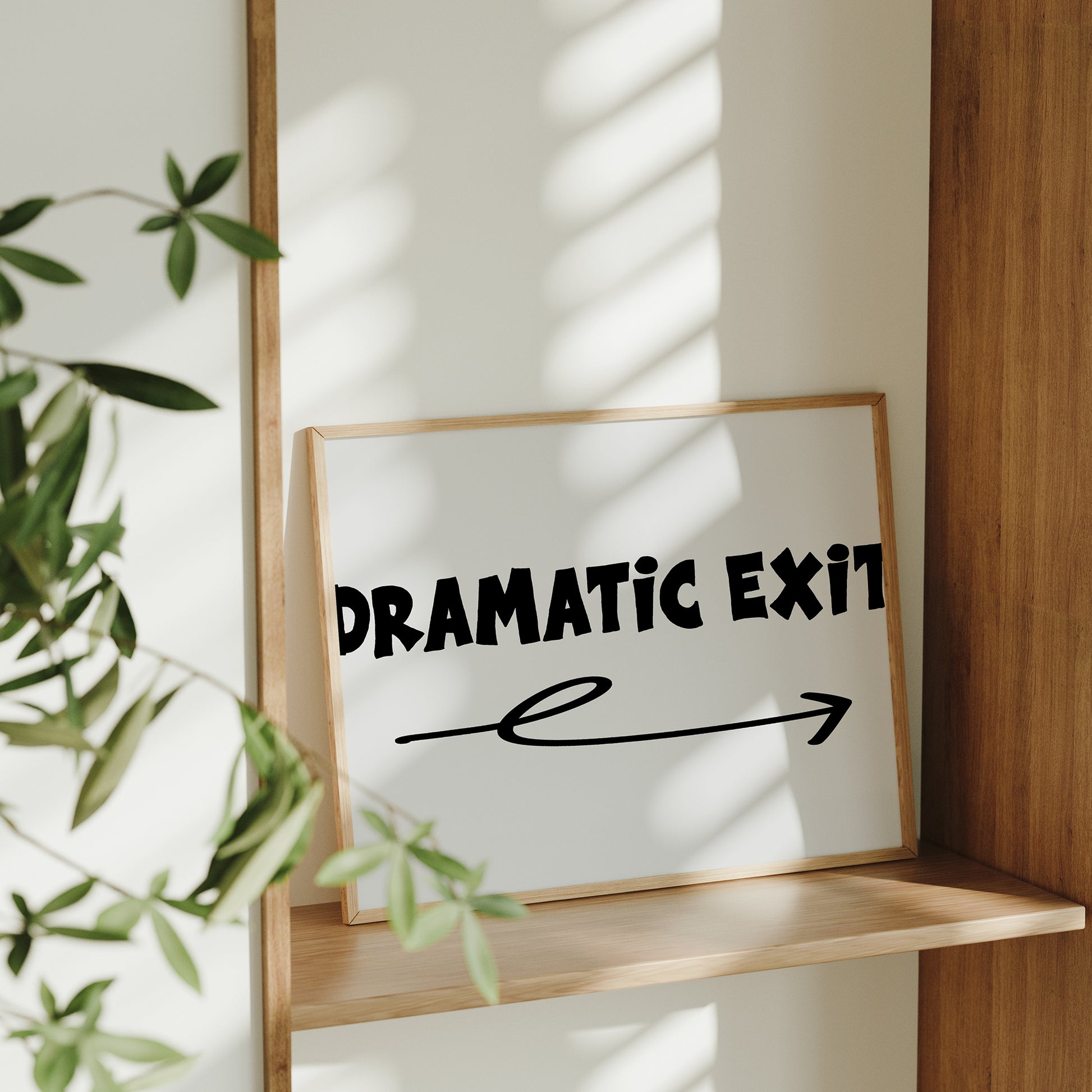 Framed DRAMATiC EXiT RiGHT poster with bold typography and arrow on shelf in sunlit modern room.