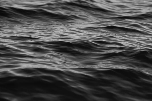 Black-and-white photograph of textured ocean waves in motion, capturing moody beauty of water - EAU NOiRE.