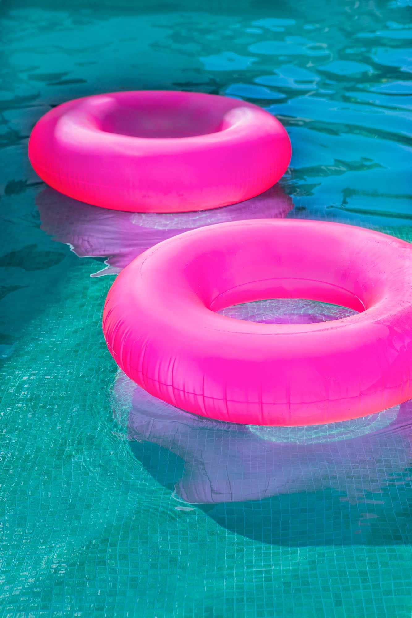 FLOATiES vibrant hot pink pool floats drifting on clear turquoise water in a bright summer scene
