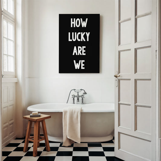 Black and white minimalist typography print poster "HOW LUCKY ARE WE" displayed in a modern bathroom setting.