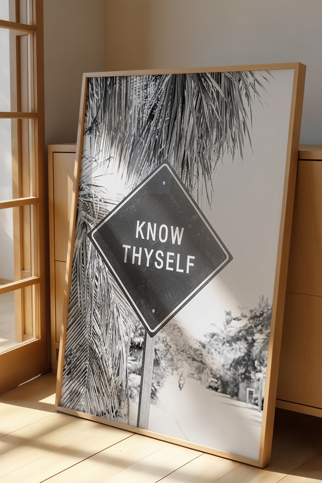 Framed black-and-white photograph titled KNOW THYSELF featuring a road sign with palm trees in a bright room.