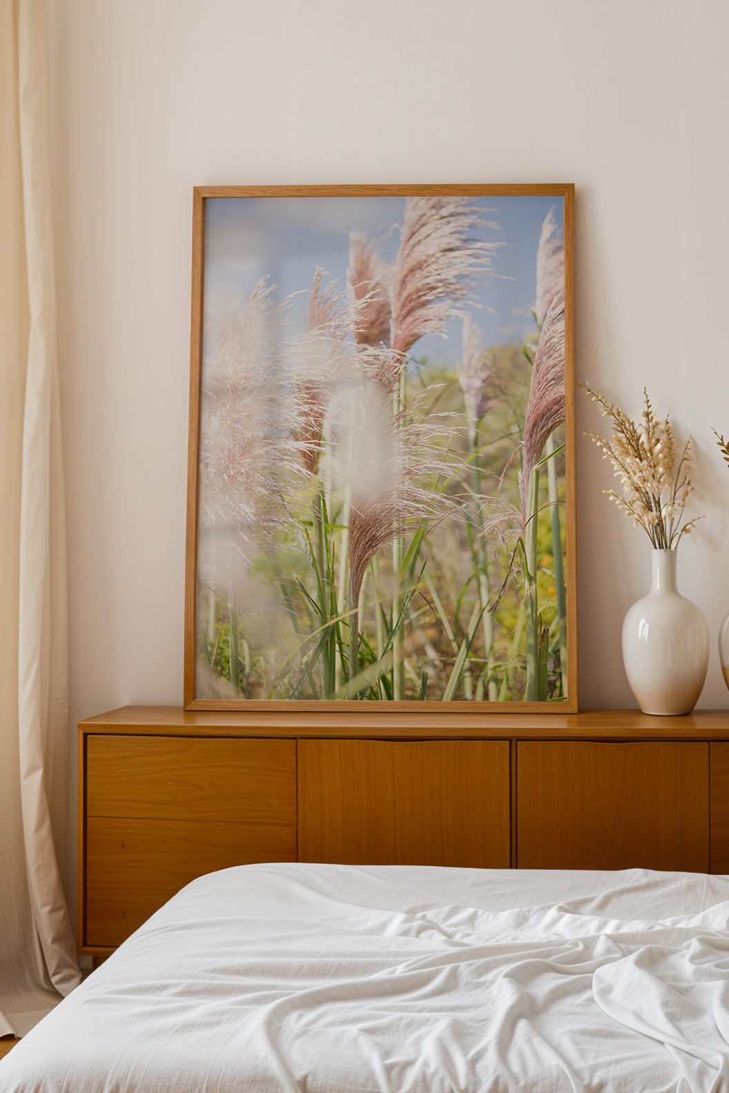 Framed photograph of pampas grass in sunlight titled LA PAMPA on wooden dresser in minimalist bedroom.