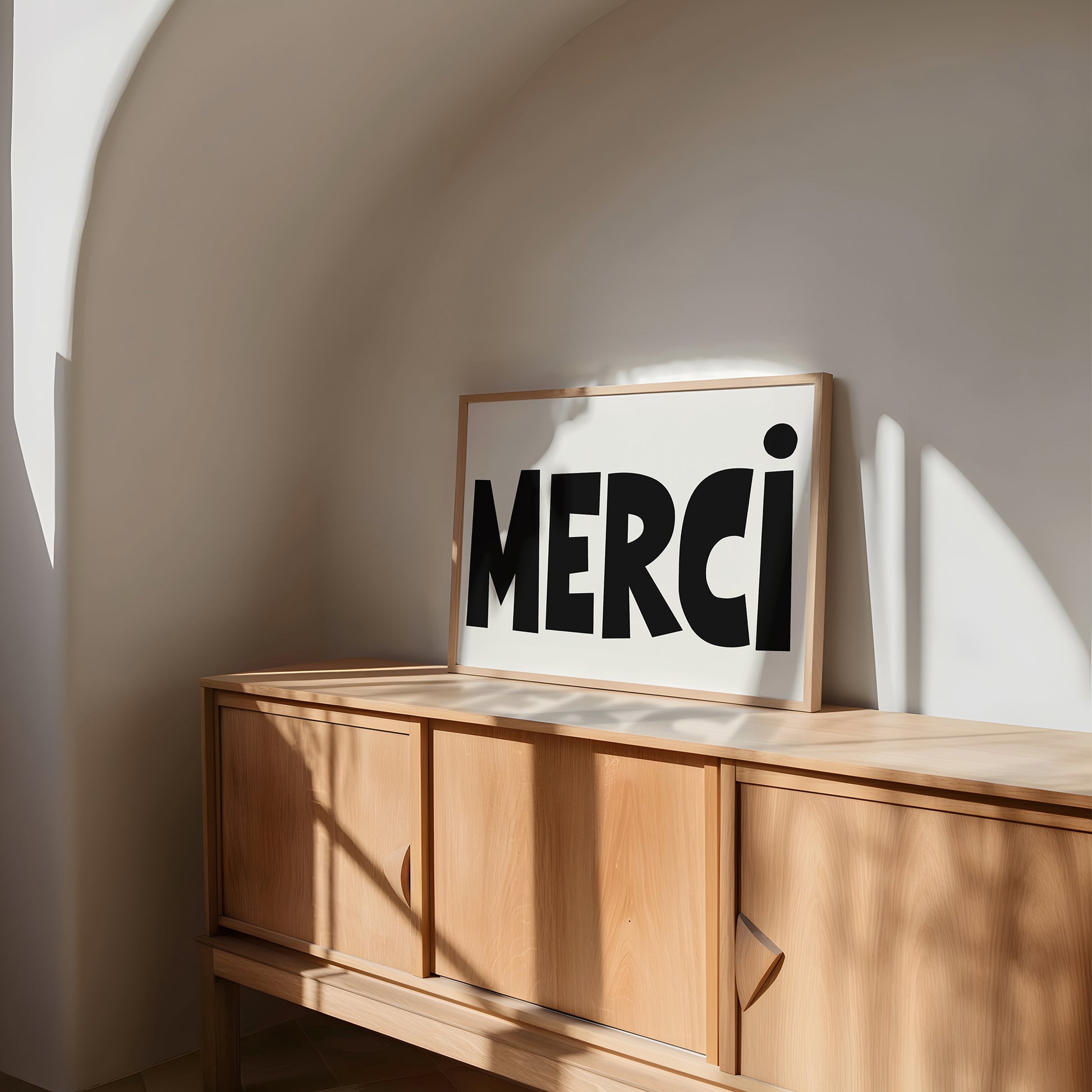 MERCi poster with bold black hand-drawn typography on white matte paper displayed on wood cabinet.