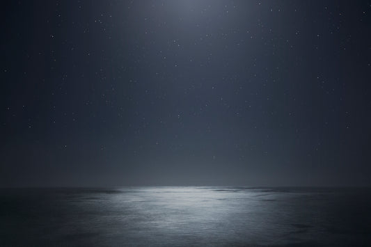 Dark ocean at night beneath a star-filled sky – moody, cosmic seascape photography