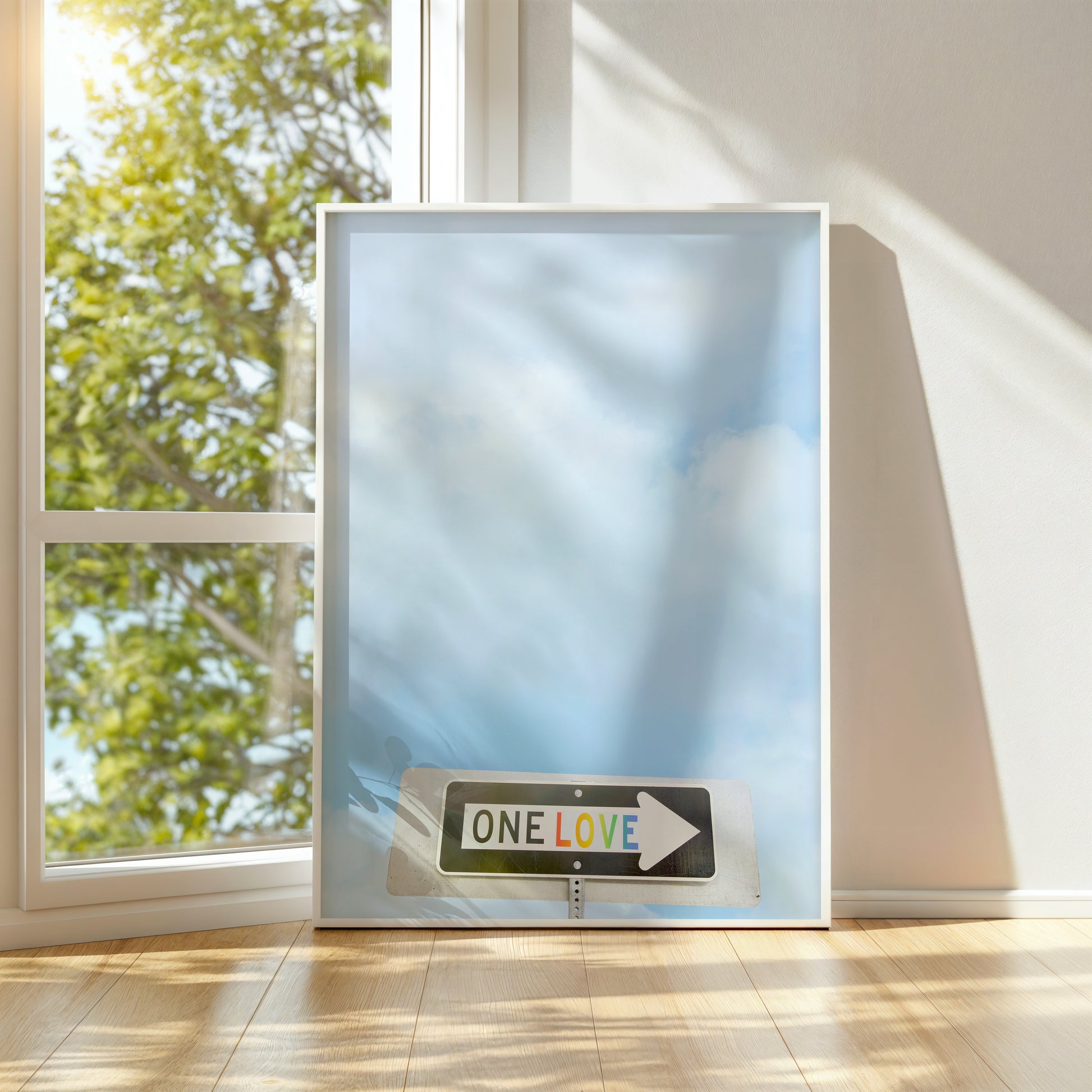 Framed photograph of a street sign with rainbow letters reading ONE LOVE against a soft blue sky background.