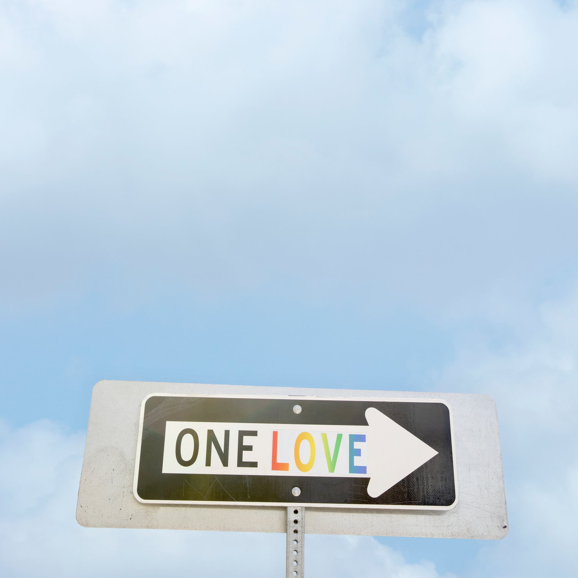 ONE LOVE street sign with rainbow letters against a sky background symbolizing unity and positivity.