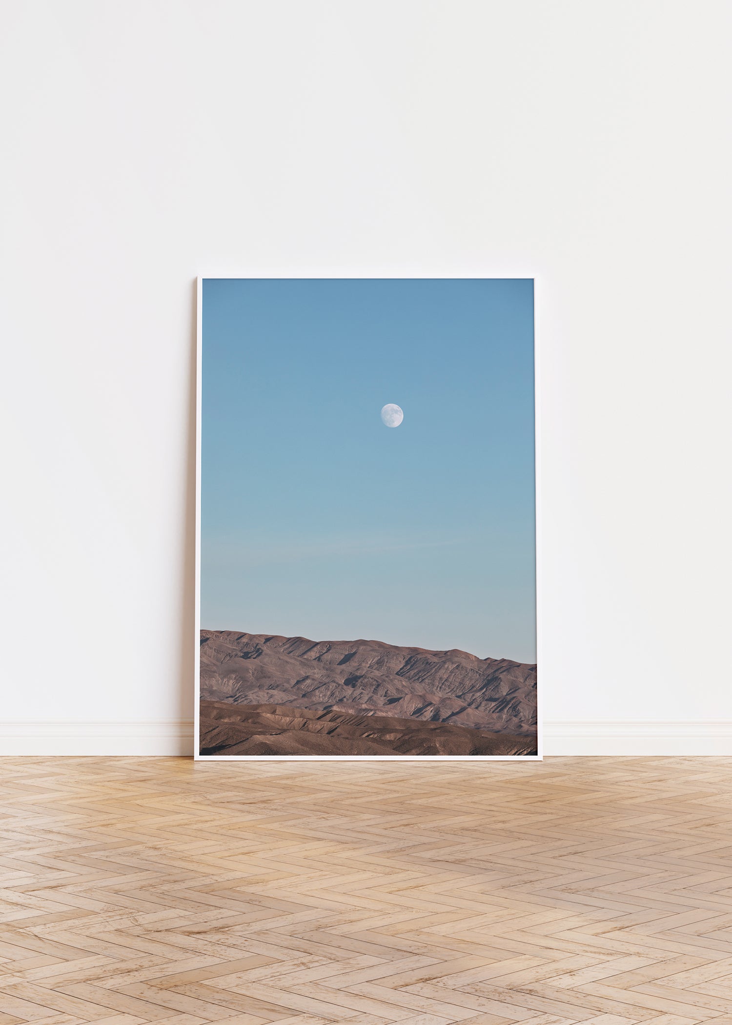RiSiNG showing moon rising over rugged desert mountains beneath a soft blue sky in a minimalist style.