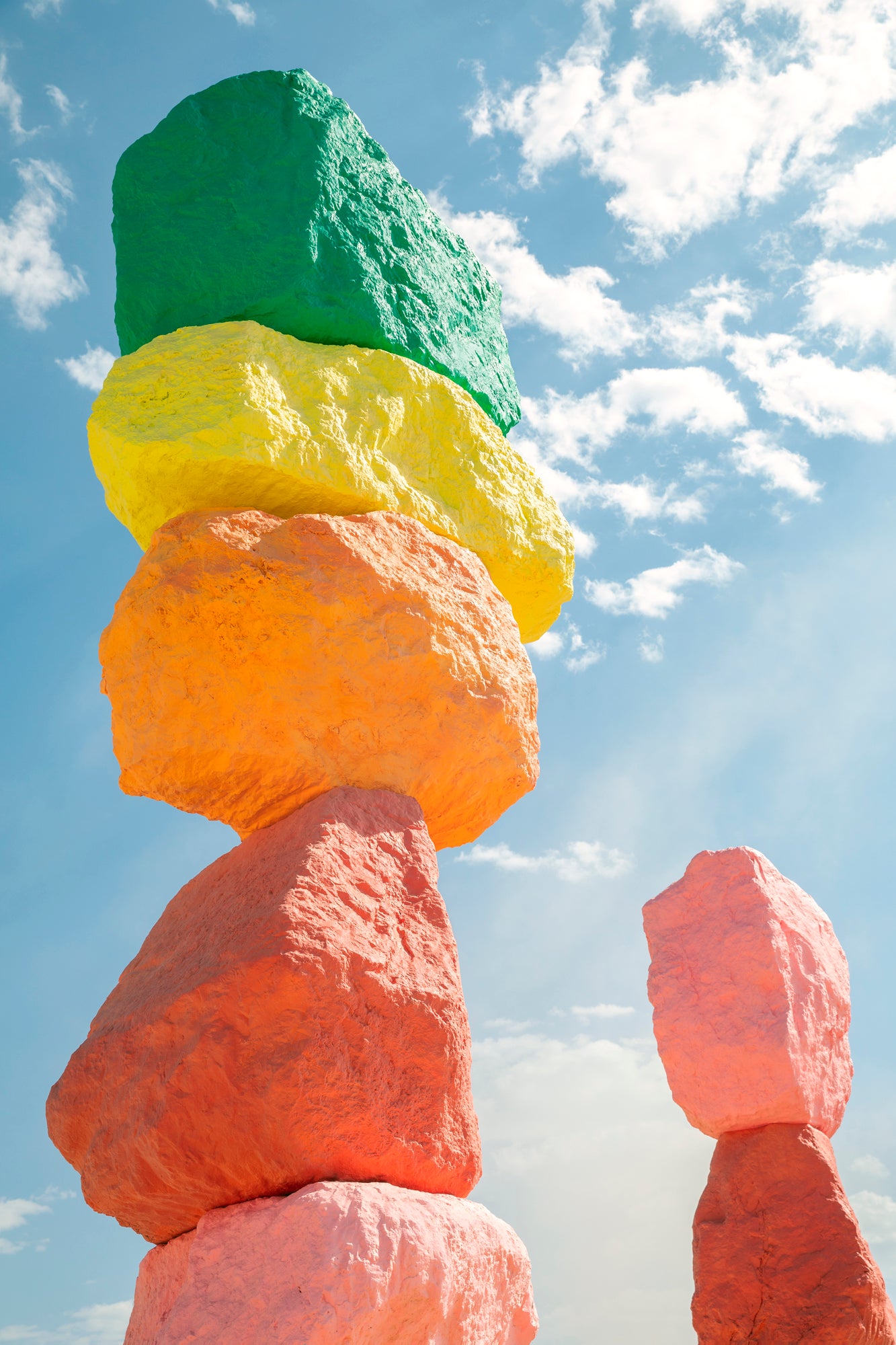 ROCK ON photograph of stacked neon-painted boulders under a bright blue sky with scattered clouds.