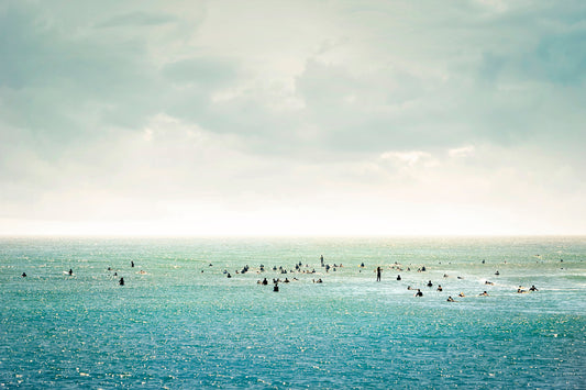 Group of surfers floating in calm water under soft pastel sky – peaceful ocean wall art