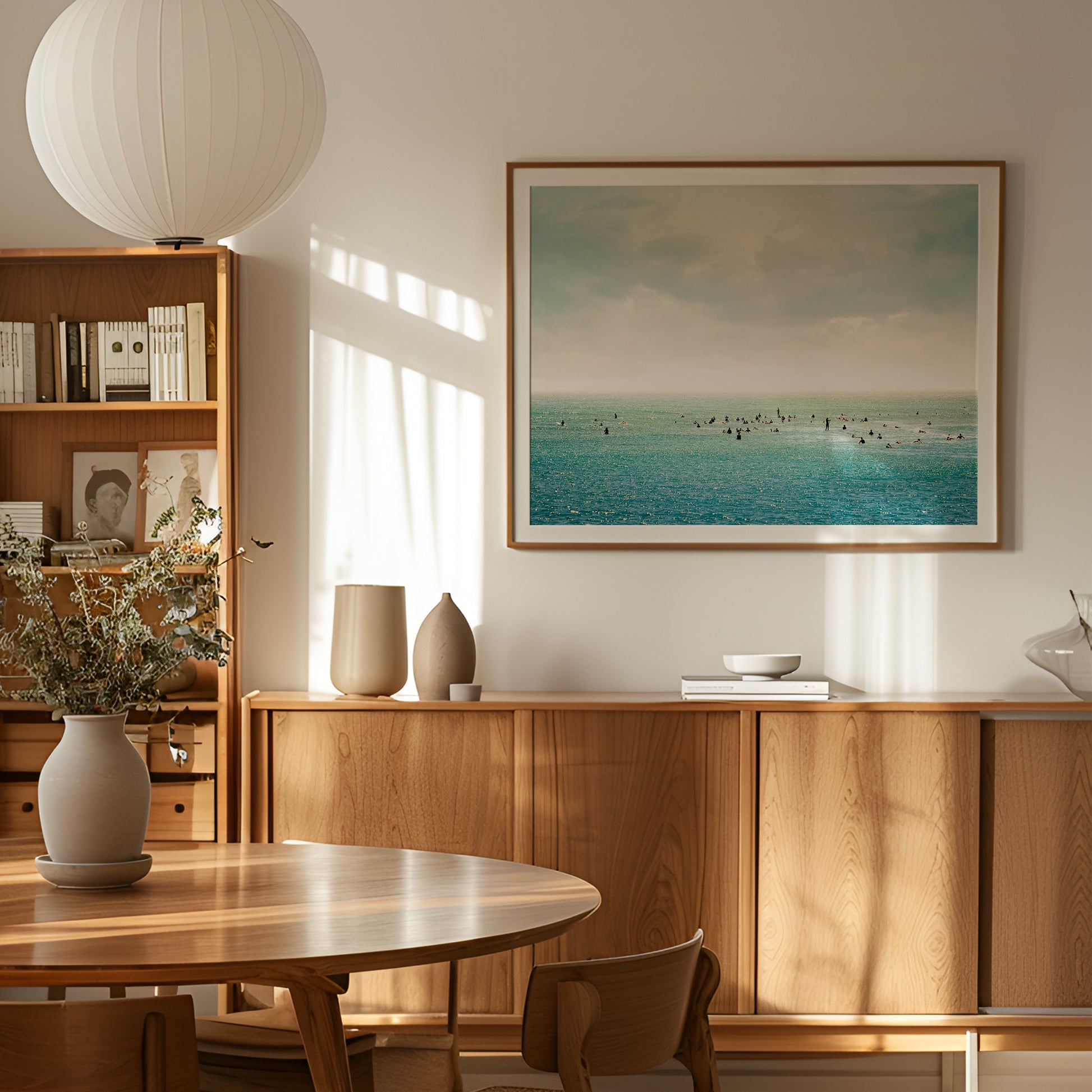 Framed SURFRiDER ocean photography showing surfers waiting in turquoise water under moody skies in a cozy modern dining room.