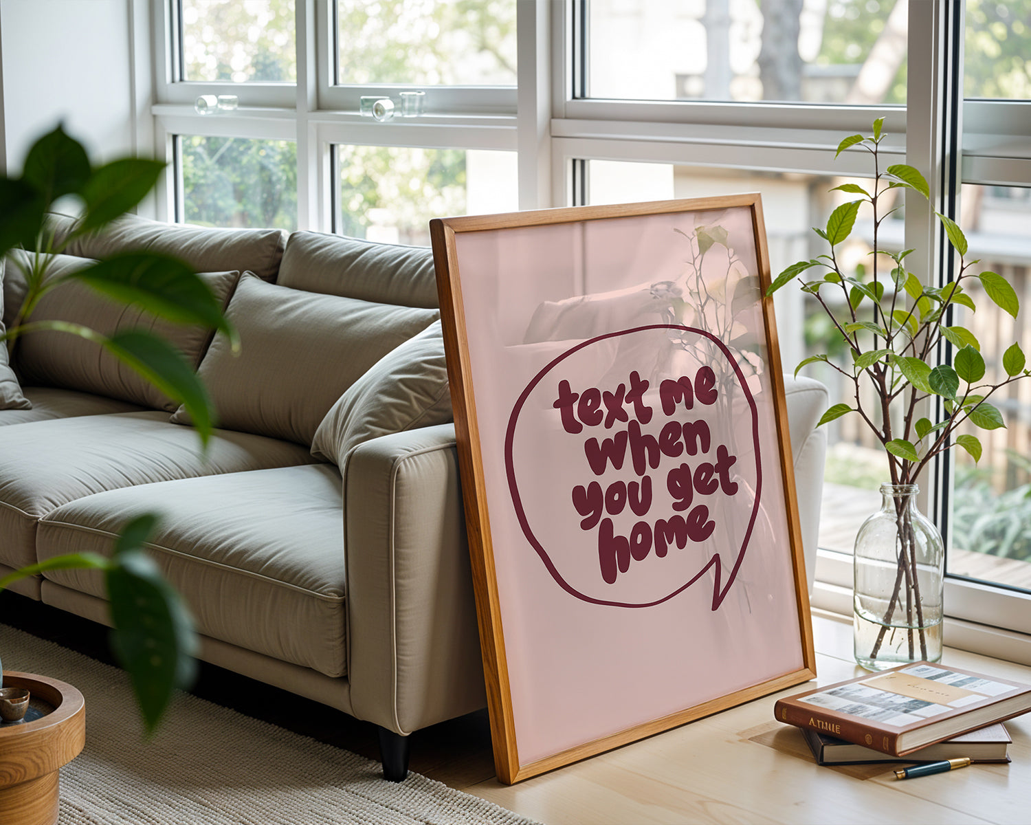 Framed "TEXT ME WHEN YOU GET HOME" poster with burgundy lettering in a speech bubble on blush background beside sofa.