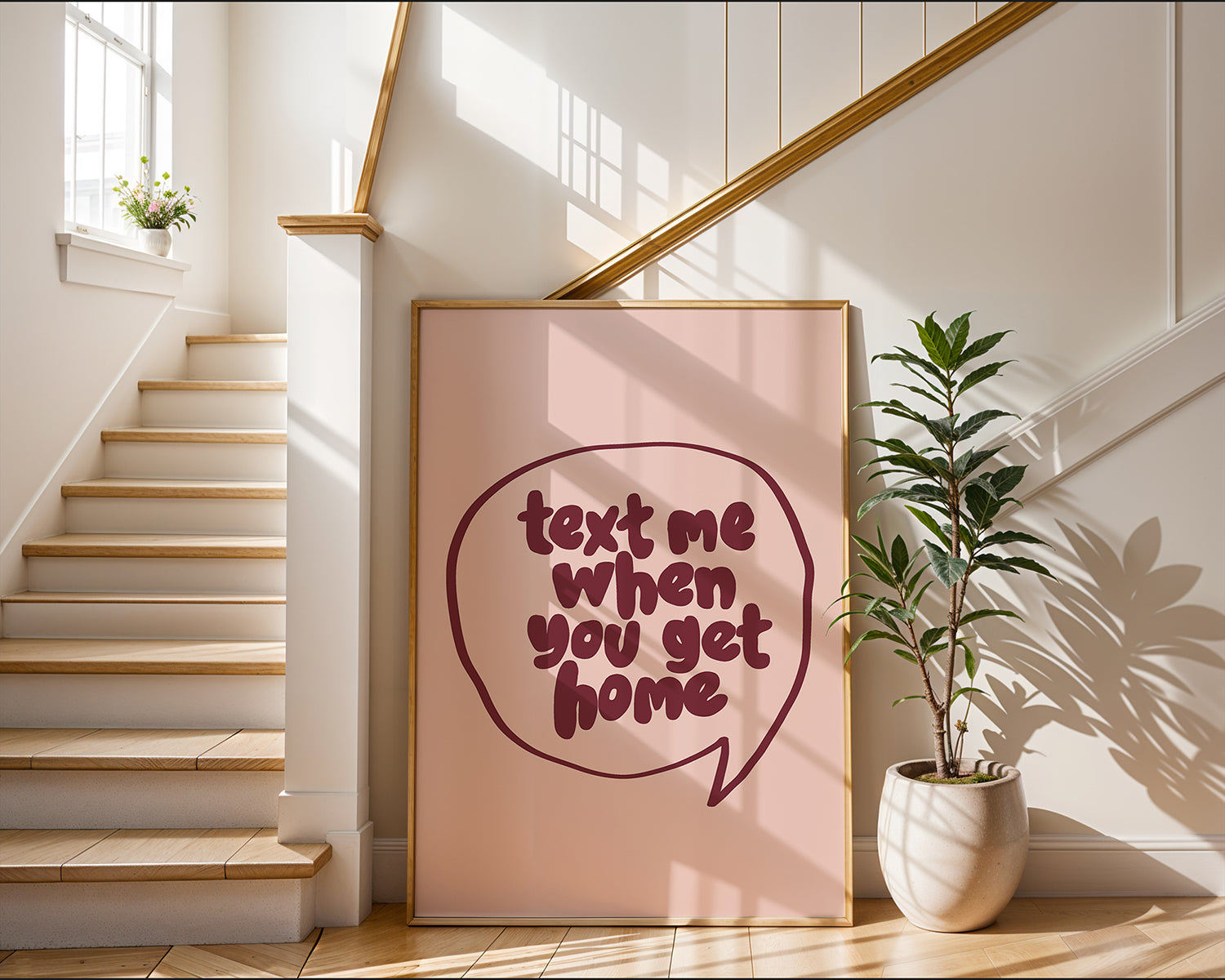 Framed poster "TEXT ME WHEN YOU GET HOME" with burgundy lettering in a speech bubble on blush background near staircase.