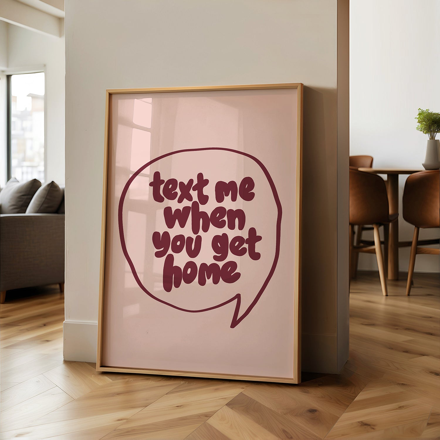 Framed "TEXT ME WHEN YOU GET HOME" poster with burgundy hand-drawn lettering on blush background leaning on wall.