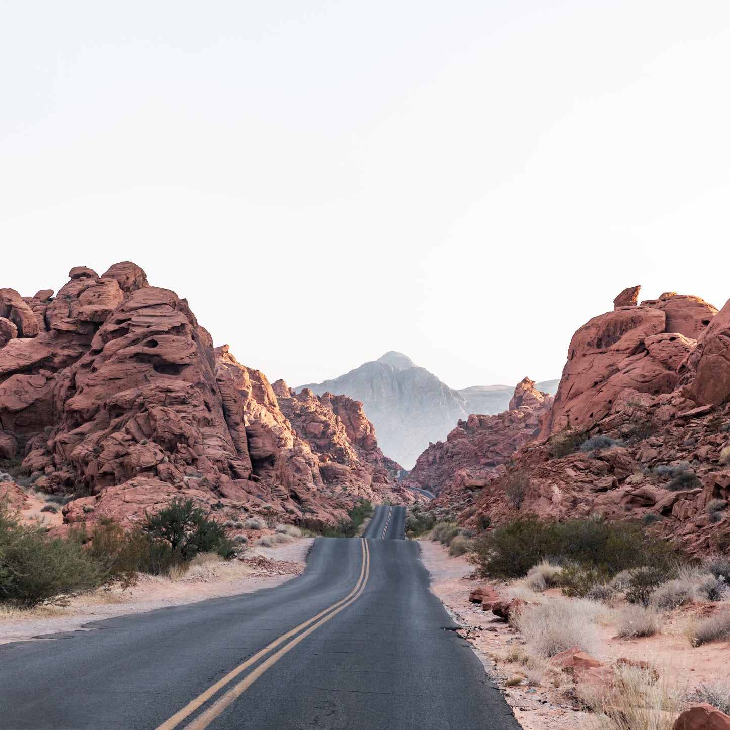 THE ROAD showing a winding desert highway surrounded by red rock formations under a clear sky.