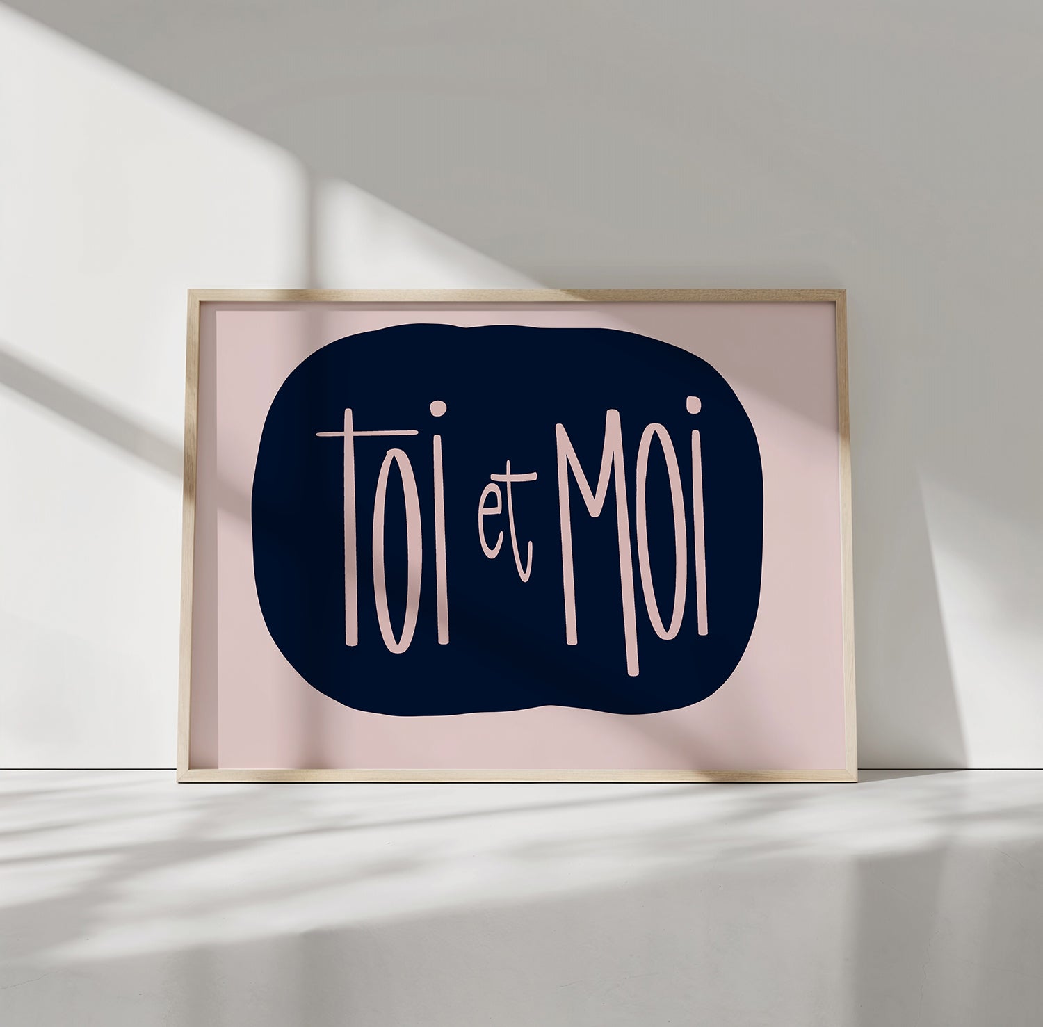 Minimalist "TOi et MOi" poster with soft blush lettering on navy background in simple wooden frame.