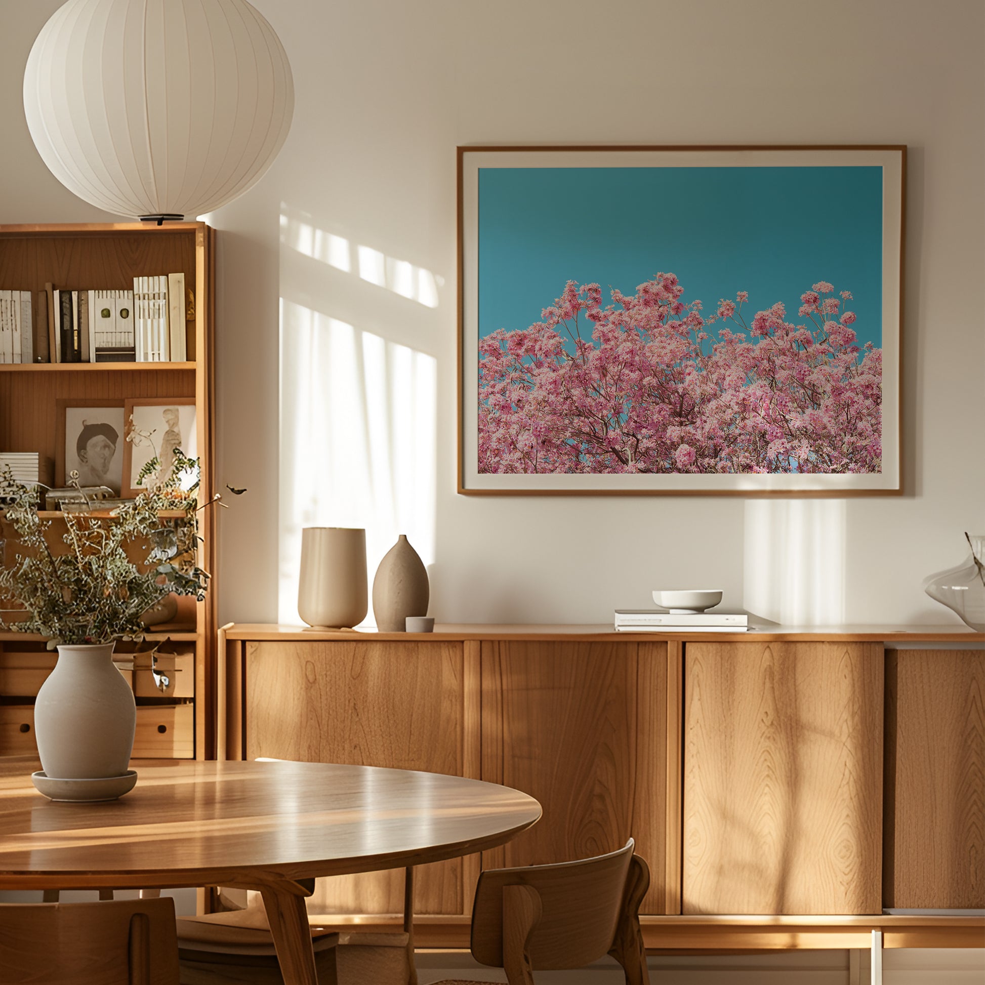 ViLLAGE BLOOM artwork showing pink blossoms against a clear blue sky in a modern, sunlit living room.