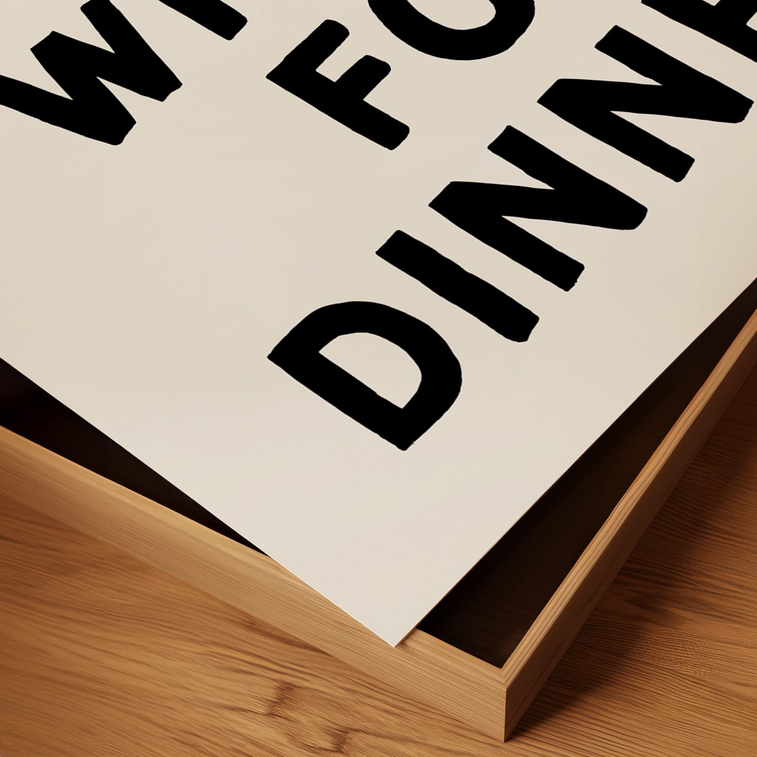Close-up of a minimalist black-and-white poster titled WHAT'S FOR DiNNER? resting in a wooden frame on a table.