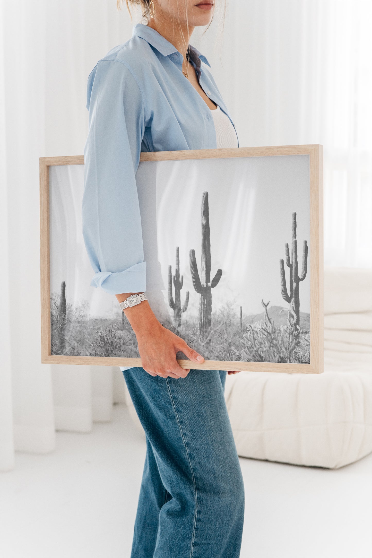 Woman holding WiLD WiLD black and white saguaro cactus print with natural wood frame in bright room