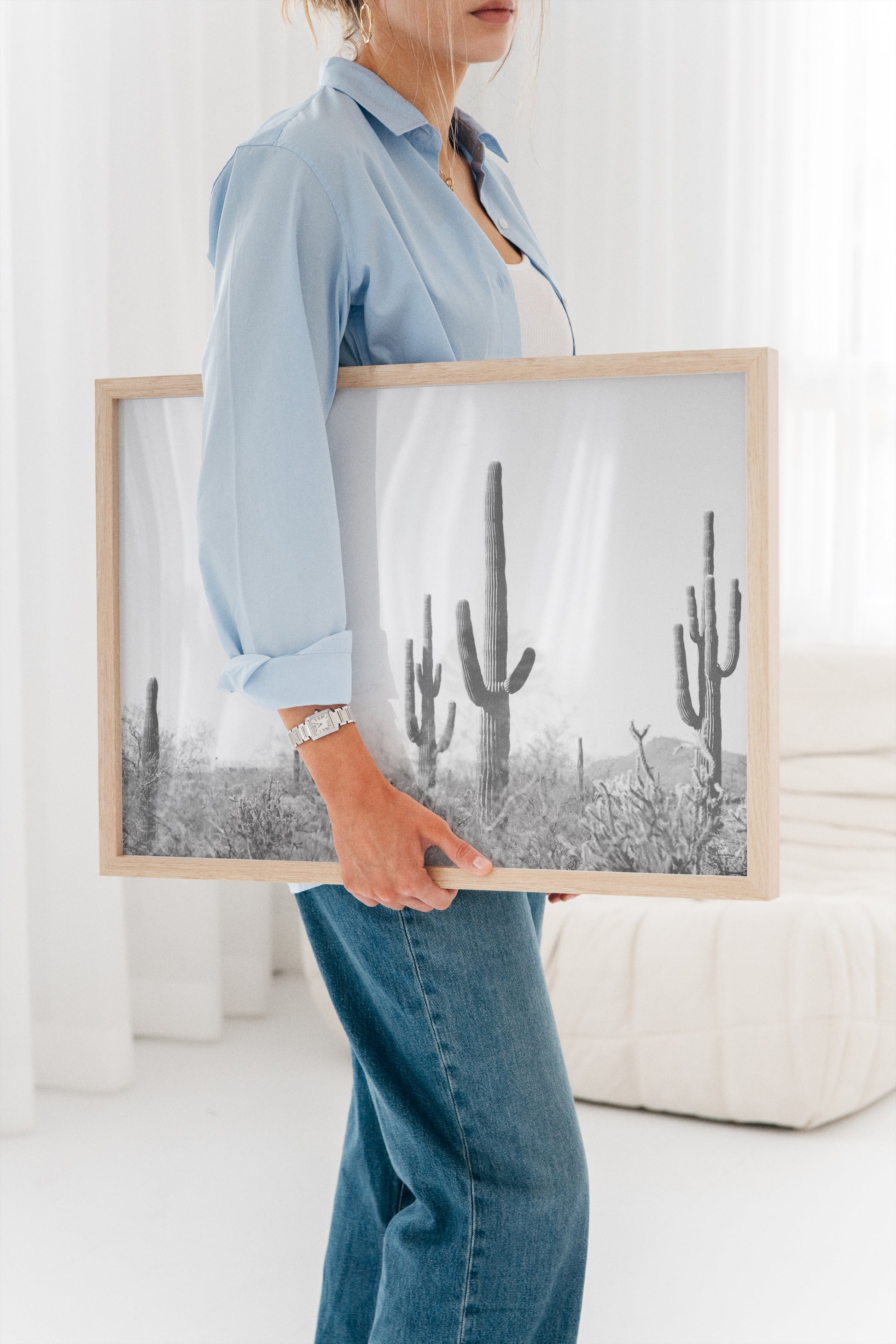 Woman holding WiLD WiLD black and white saguaro cactus print with natural wood frame in bright room