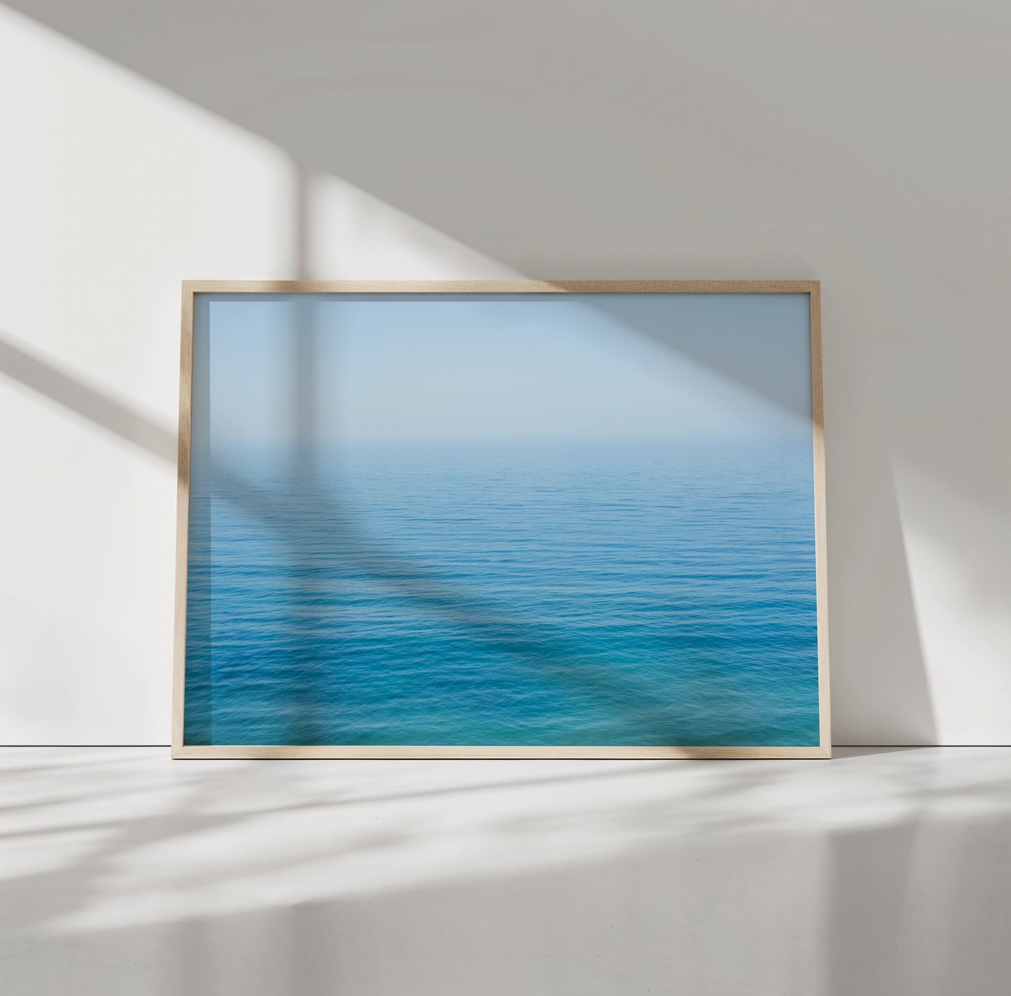 Minimalist ocean print of calm blue and turquoise water with endless horizon titled YOU ARE SMALL in a light wood frame.