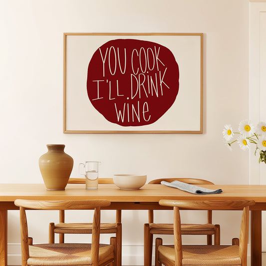Framed "YOU COOK I'LL DRINK WiNE" poster in burgundy on white, displayed above wooden dining table with chairs.