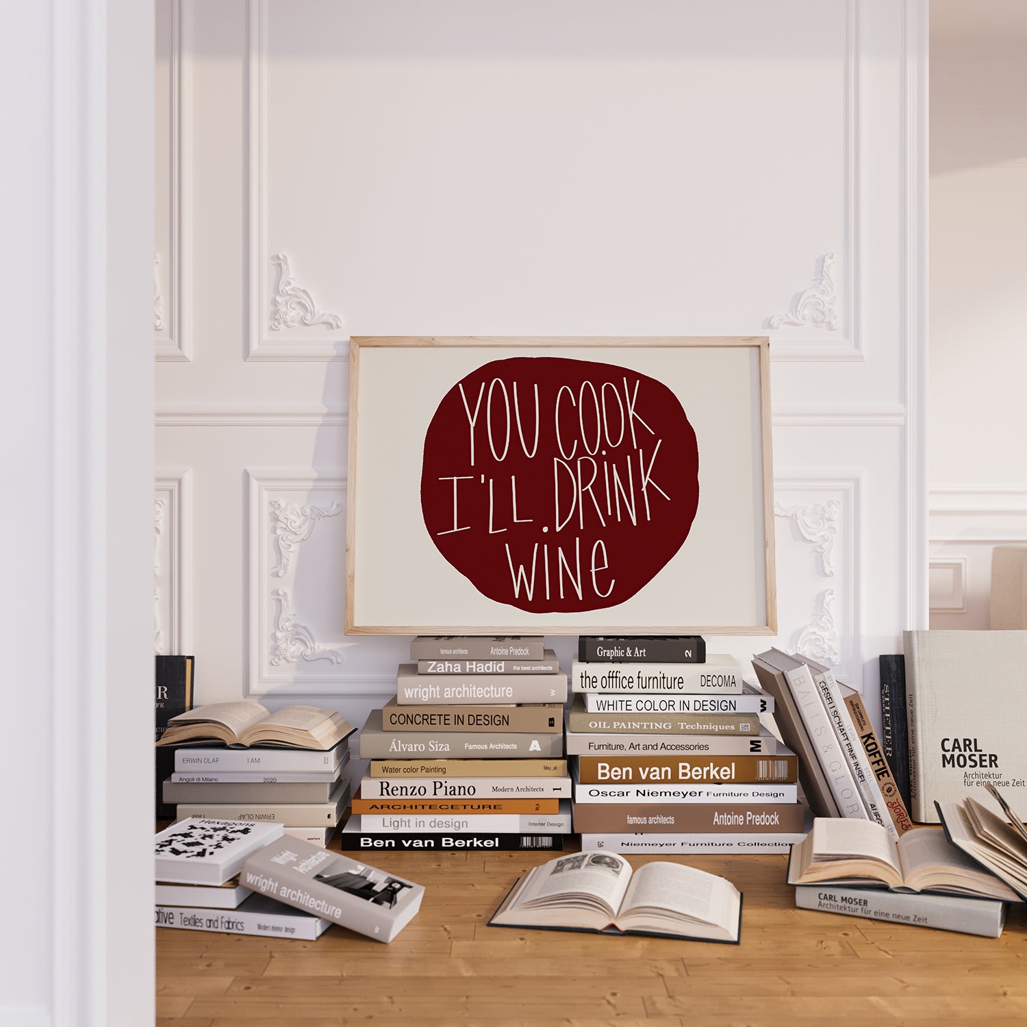 YOU COOK I'LL DRINK WiNE poster in deep red burgundy typography displayed above a stack of design books.