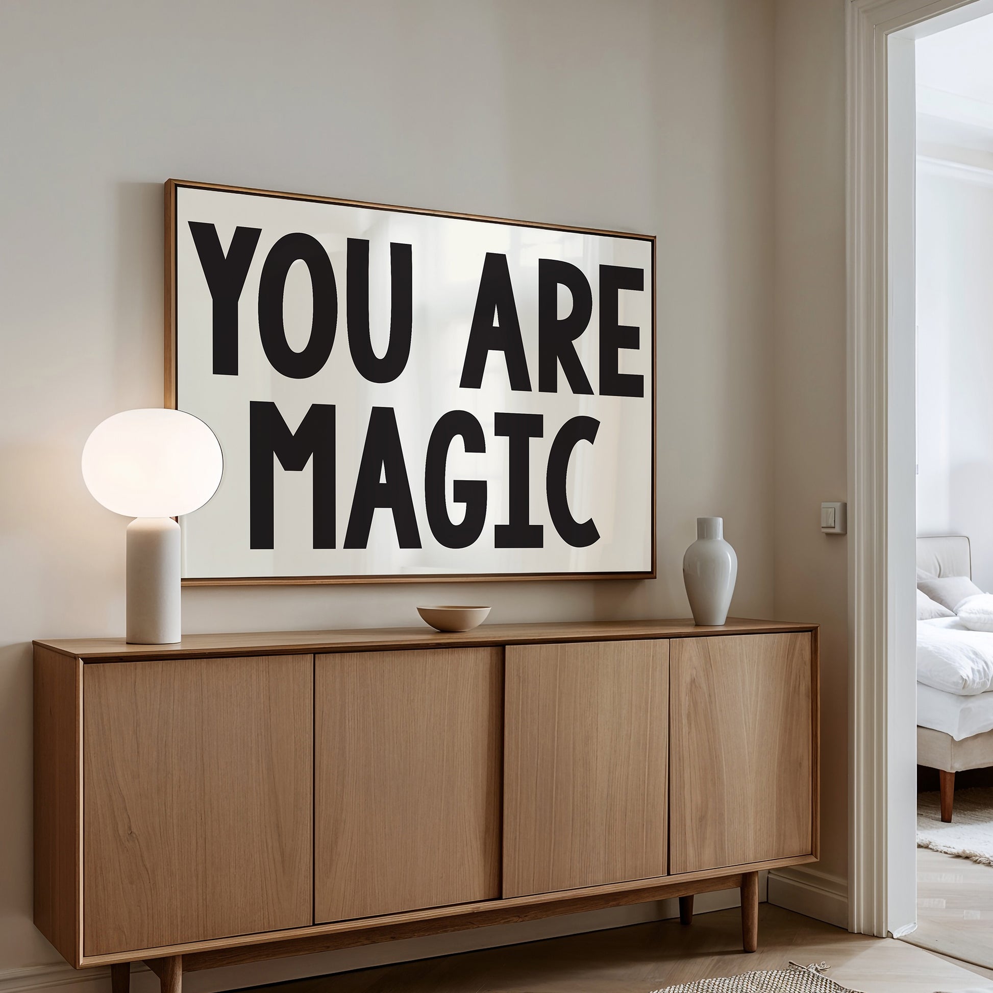 YOU ARE MAGiC poster with bold black typography on white background displayed above a wooden sideboard in a modern room.