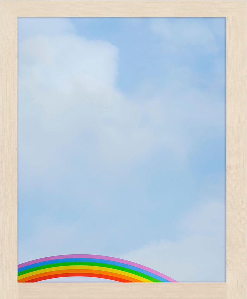 A rainbow peeks up into an image of a soft blue cloudy sky