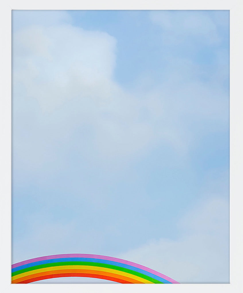 A rainbow peeks up into an image of a soft blue cloudy sky